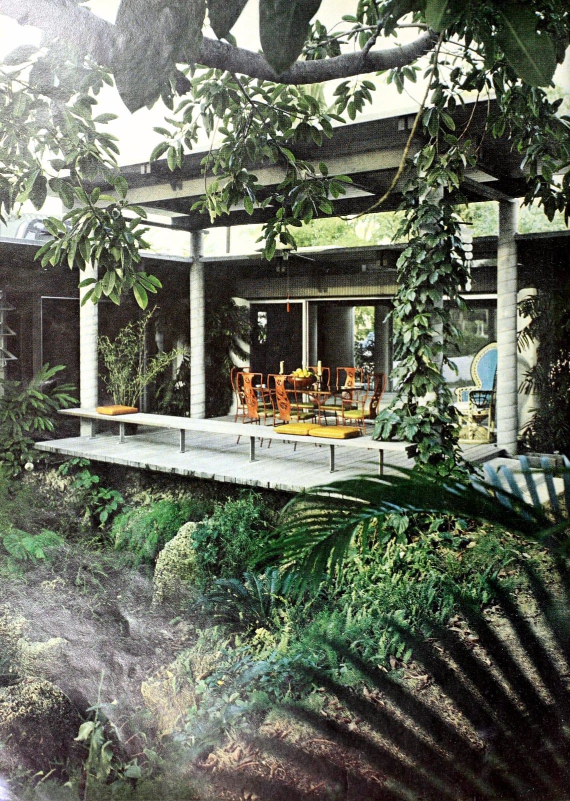 A simple low wooden patio deck set in a lush mid century modern style backyard